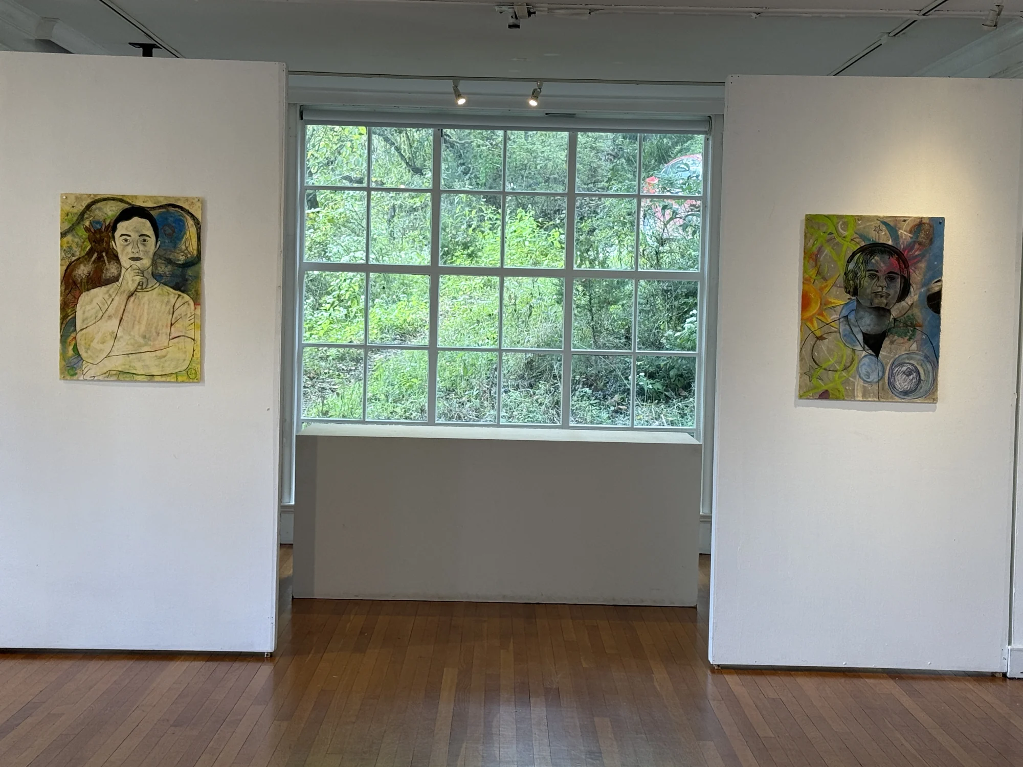 Two self-portrait drawings displayed on either side of a gallery window.