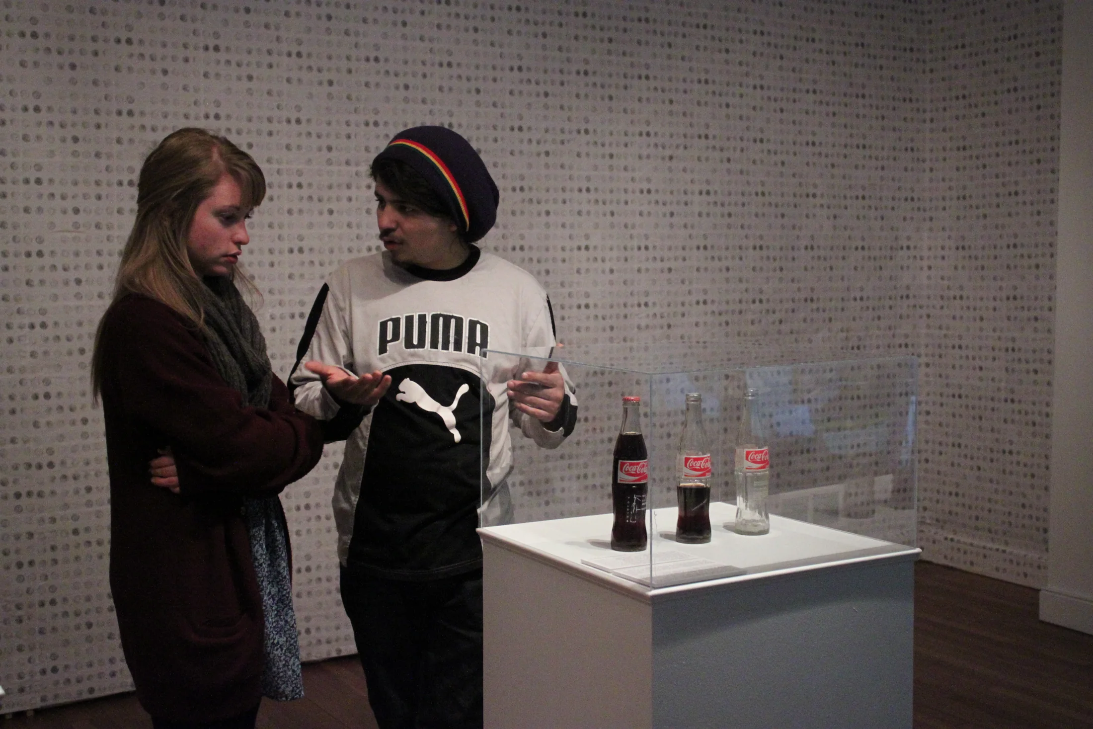 Gallery exhibition view with visitors and artwork.